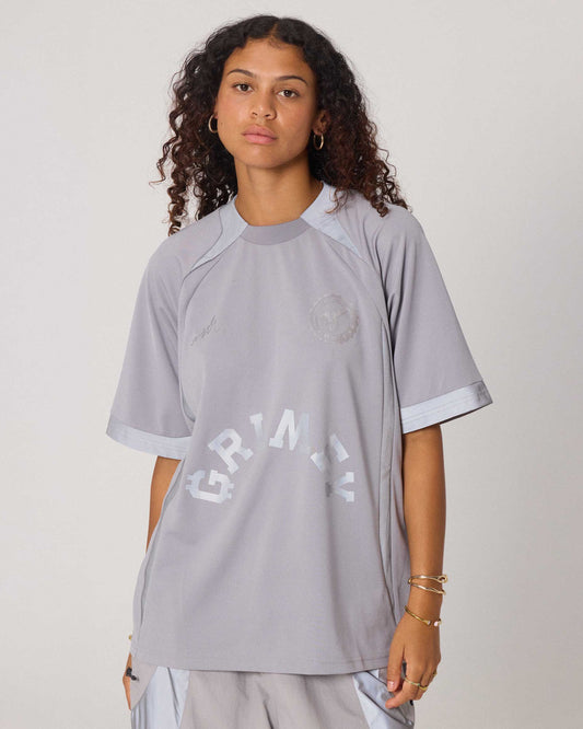 Camiseta de fútbol gris The Infamous de la marca Grimey, diseño con detalles deportivos y logotipo en el pecho.